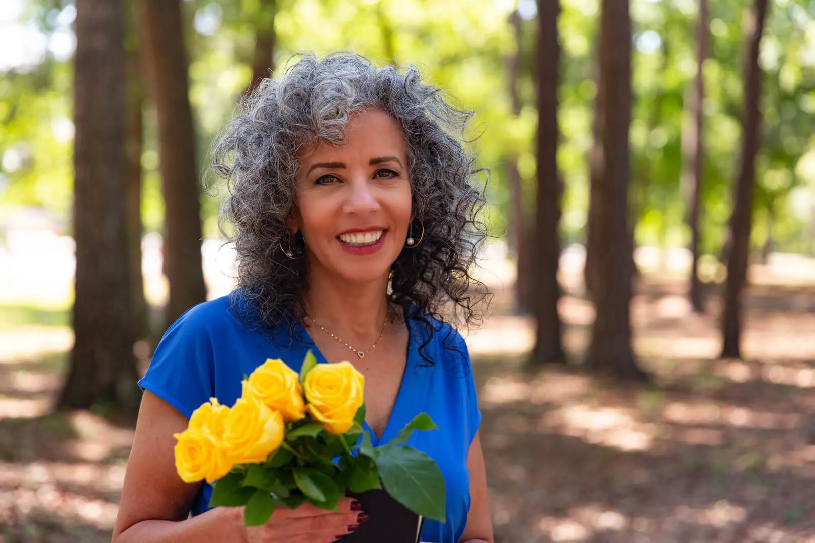 Woman smiling holding yellow roses in forest.